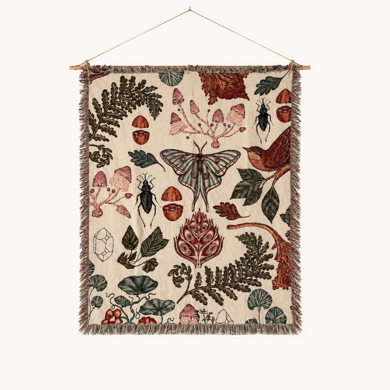 Vintage botanical woven wall tapestry featuring mushrooms, a moth, beetles, birds, leaves, flowers, and fringe on a cream background.