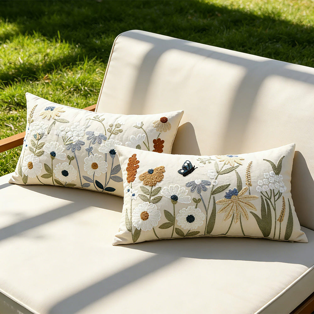 Two embroidered wildflower pillow covers styled on a sunlit cushioned bench