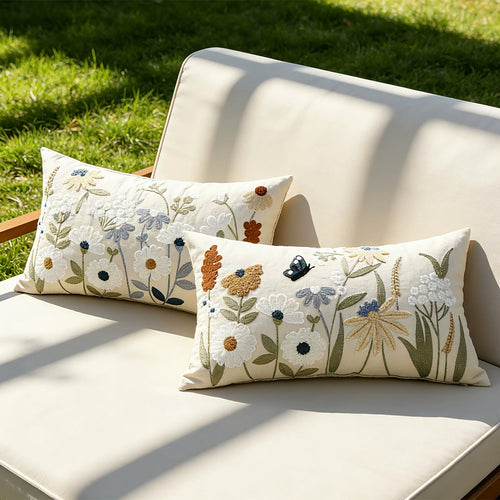 Two embroidered wildflower pillow covers styled on a sunlit cushioned bench