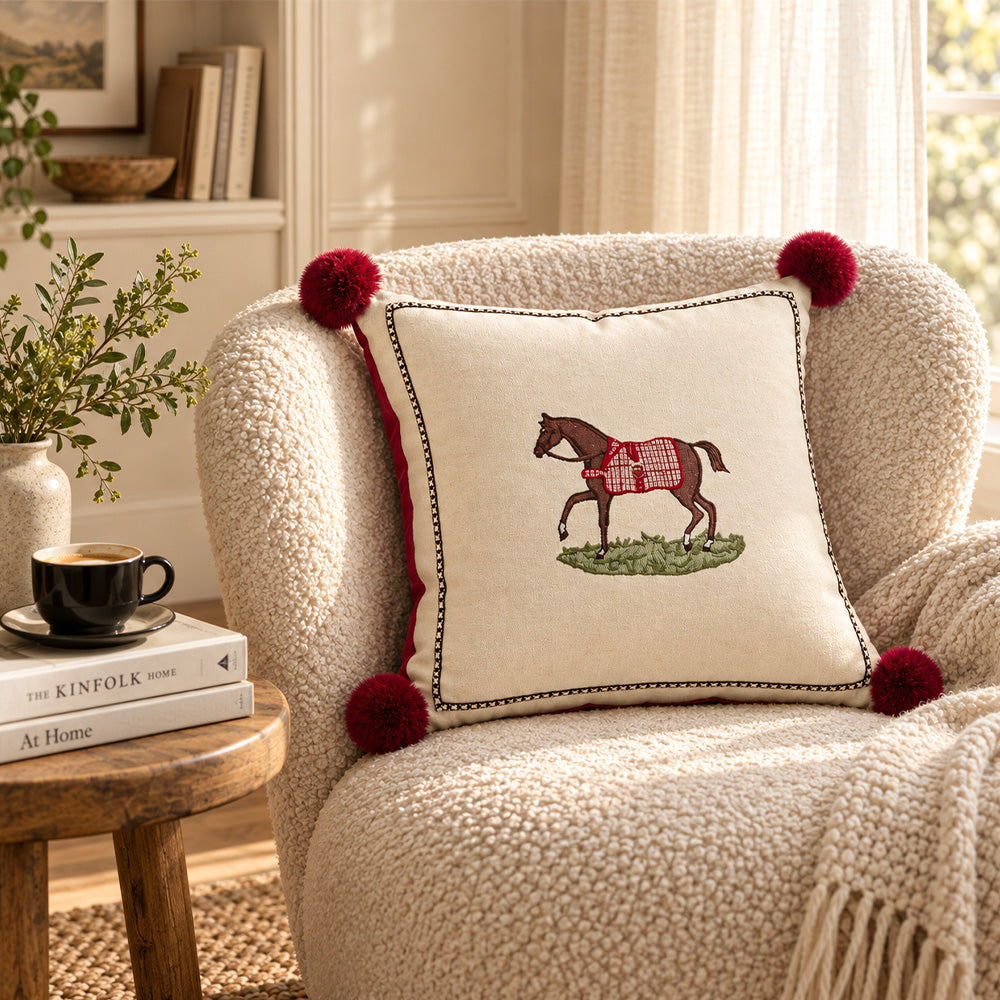 Redbrook embroidered horse pom pom pillow cover styled on a cream boucle armchair