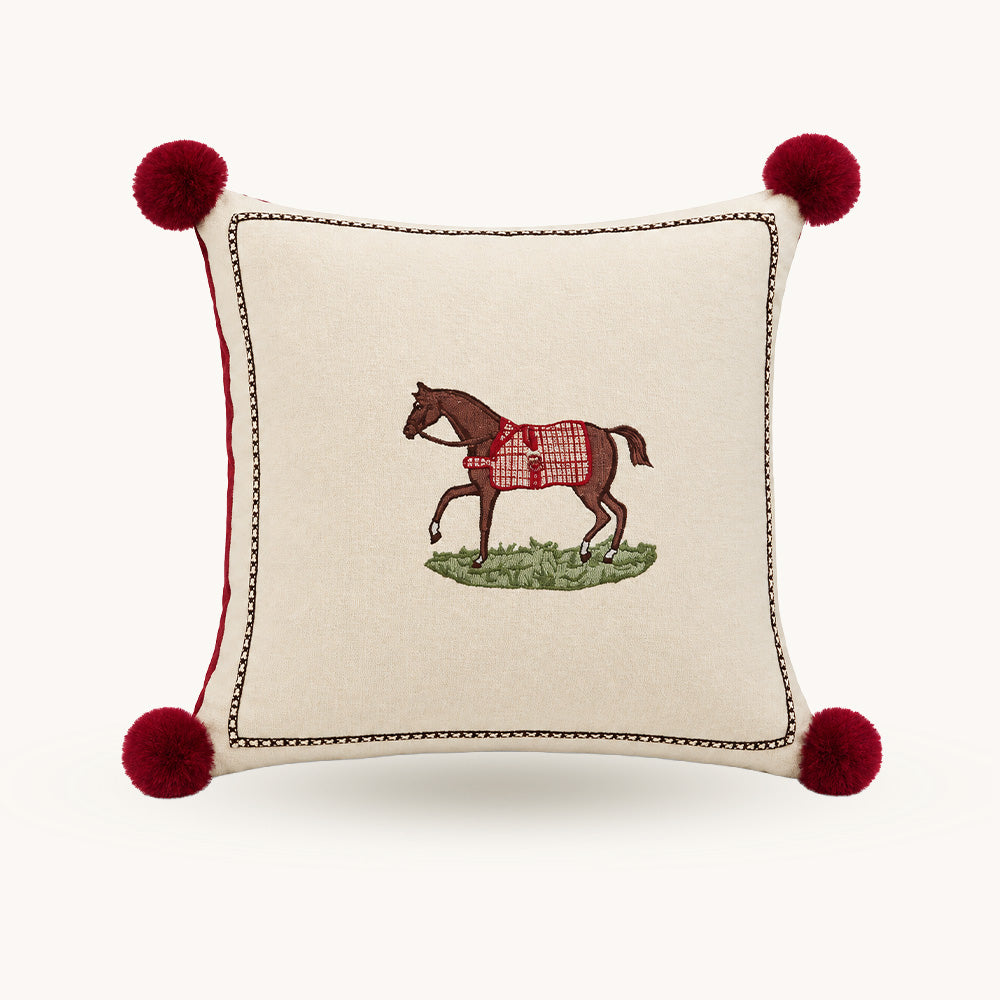 Front view of Redbrook cream 18x18 pillow cover with embroidered horse and red pom pom corners