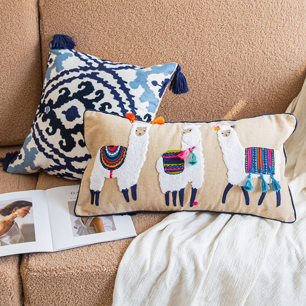 Blue tassel pillow cover paired with a llama lumbar pillow on a beige sofa.