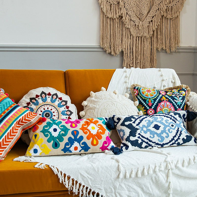 Collection of embroidered bohemian pillow covers in floral, geometric, and tassel designs displayed on a sofa.