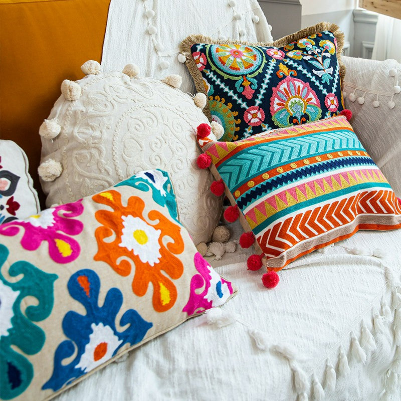 Assorted embroidered boho decorative pillows layered on a white textured sofa with colorful accent cushions.