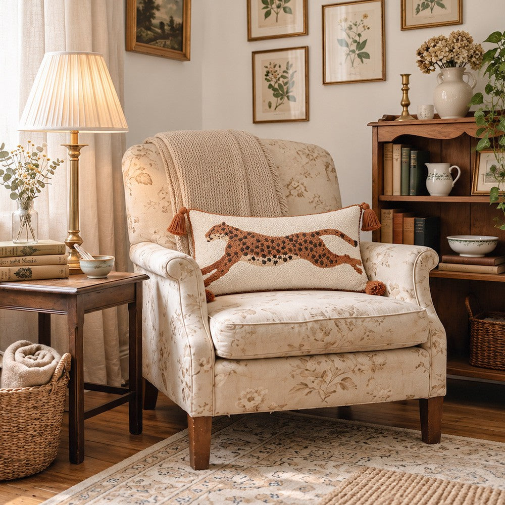 A cream floral armchair in a cozy, decorated living room, featuring a decorative throw pillow with a brown spotted leopard design.