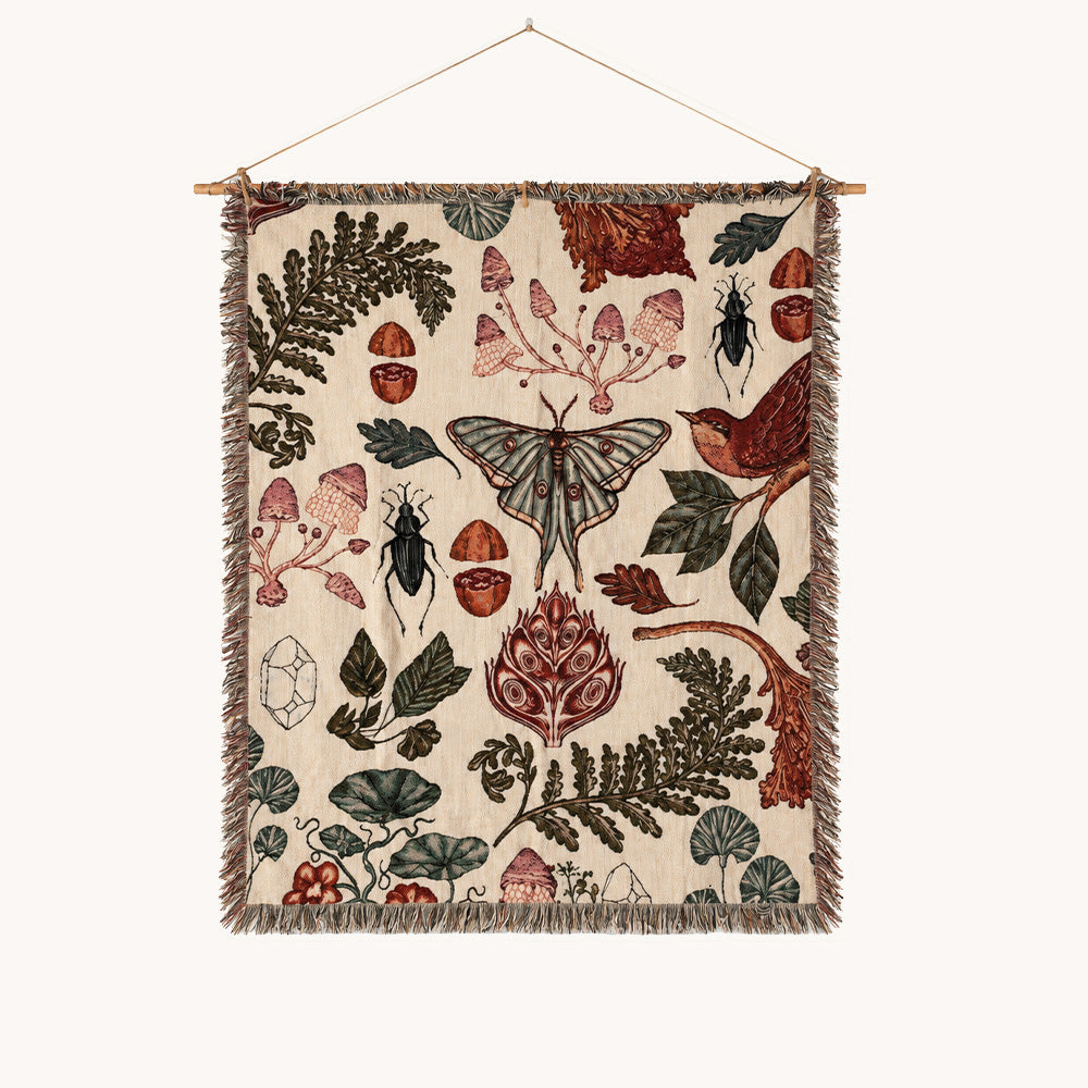 Vintage botanical woven wall tapestry featuring mushrooms, a moth, beetles, birds, leaves, flowers, and fringe on a cream background.